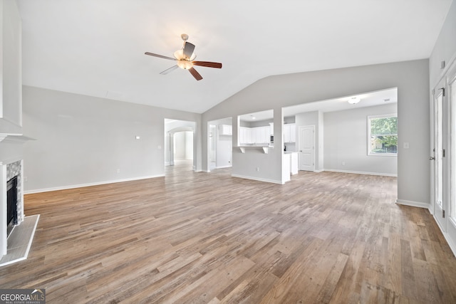 unfurnished living room with vaulted ceiling, light wood-style floors, a ceiling fan, a high end fireplace, and arched walkways
