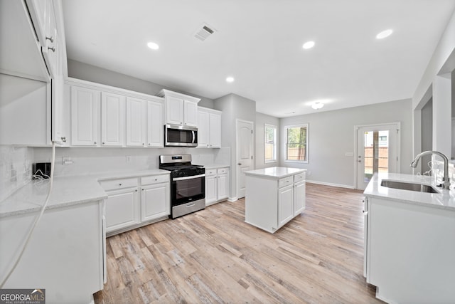 kitchen with a sink, light wood finished floors, white cabinetry, a center island, and stainless steel appliances