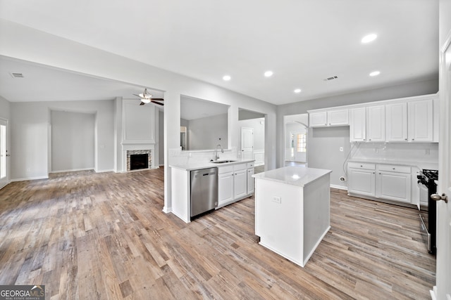 kitchen featuring light countertops, stainless steel dishwasher, a sink, ceiling fan, and a stone fireplace