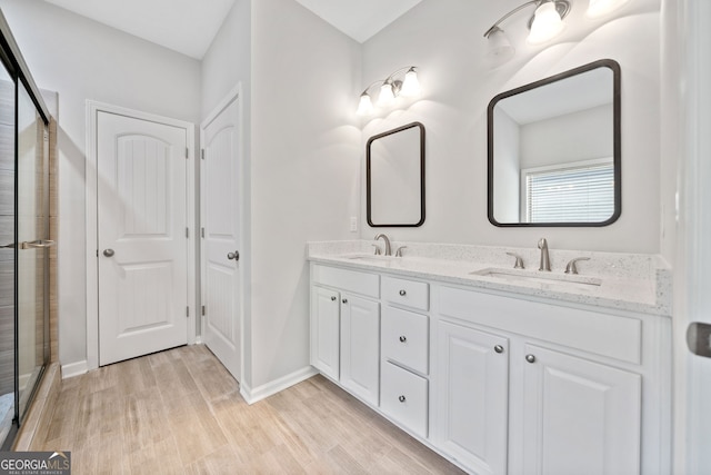 full bath with double vanity, a sink, a tile shower, and wood finished floors