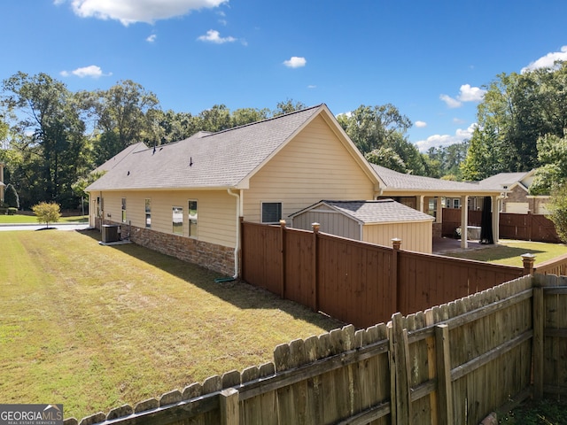 view of property exterior featuring stone siding, roof with shingles, central air condition unit, a fenced backyard, and a yard