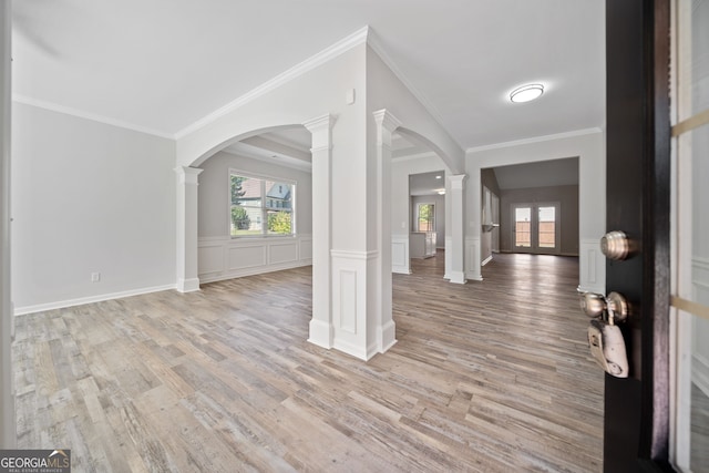 entryway featuring decorative columns, arched walkways, light wood finished floors, and wainscoting
