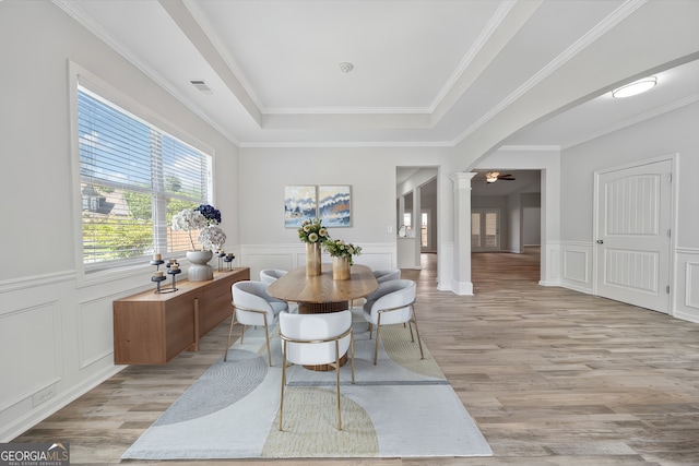 dining area with decorative columns, light wood-style flooring, a wainscoted wall, and a raised ceiling