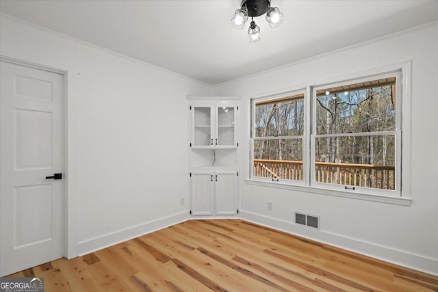 empty room with visible vents, baseboards, ornamental molding, and light wood-style flooring