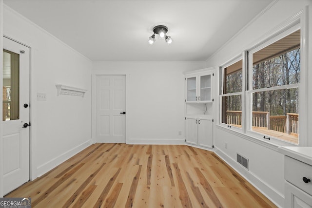 unfurnished dining area featuring light wood finished floors, baseboards, ornamental molding, and visible vents