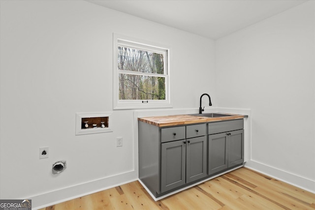 laundry room with hookup for a washing machine, hookup for an electric dryer, a sink, light wood finished floors, and baseboards