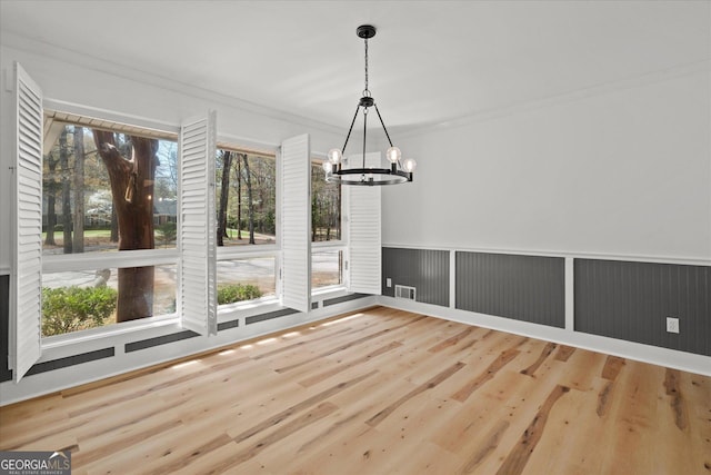 unfurnished dining area with ornamental molding, visible vents, a wainscoted wall, wood finished floors, and a notable chandelier