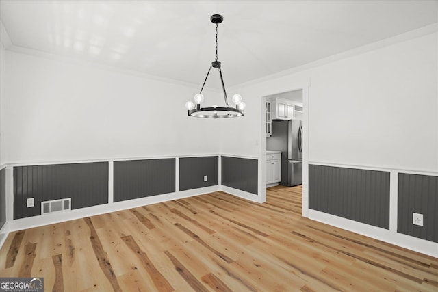 unfurnished dining area featuring light wood-style flooring, wainscoting, visible vents, a chandelier, and crown molding