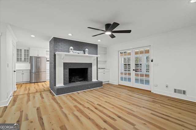 unfurnished living room featuring a fireplace, light wood-style flooring, a ceiling fan, visible vents, and french doors