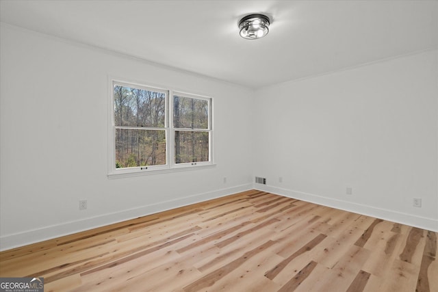 spare room with ornamental molding, baseboards, wood finished floors, and visible vents