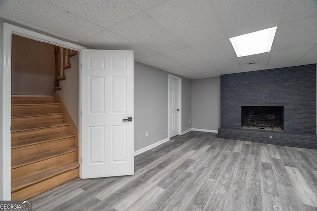 unfurnished living room with stairway, a brick fireplace, a drop ceiling, and wood finished floors