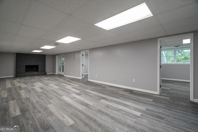 unfurnished living room featuring baseboards, a paneled ceiling, wood finished floors, and a fireplace