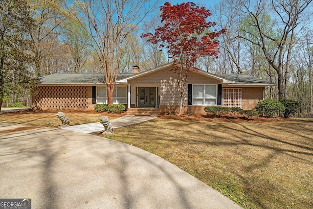 ranch-style house featuring a chimney, brick siding, a front yard, and french doors