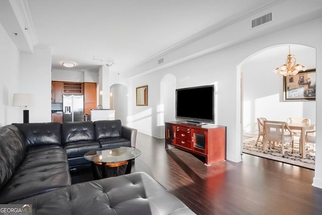 living room featuring crown molding, arched walkways, a chandelier, wood finished floors, and visible vents