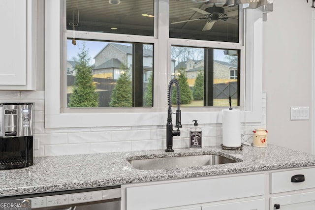 kitchen with light stone counters, backsplash, dishwasher, a sink, and white cabinetry