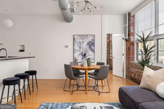 dining space with baseboards, a notable chandelier, light wood-style flooring, and brick wall