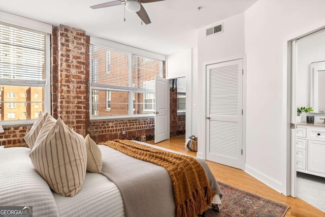 bedroom featuring light wood-style floors, visible vents, multiple windows, and brick wall