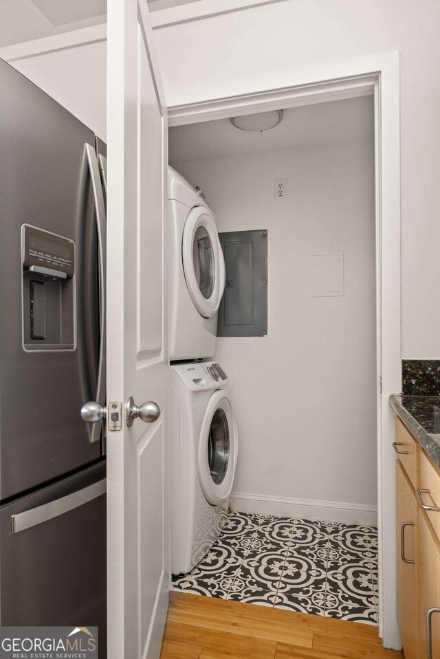 laundry room featuring wood finished floors, baseboards, stacked washer and dryer, laundry area, and electric panel