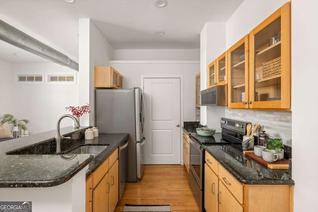 kitchen with light wood-type flooring, backsplash, a sink, a peninsula, and appliances with stainless steel finishes
