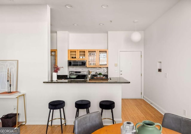 kitchen with a breakfast bar area, tasteful backsplash, appliances with stainless steel finishes, a peninsula, and glass insert cabinets