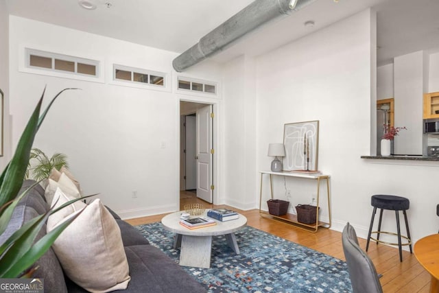 living area with baseboards, wood finished floors, and beam ceiling