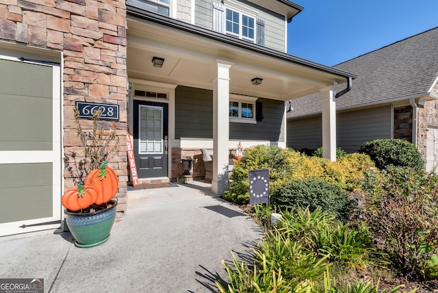 doorway to property featuring a porch, a shingled roof, and stone siding