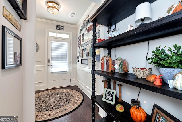doorway to outside with crown molding, visible vents, a wainscoted wall, dark wood-type flooring, and a decorative wall