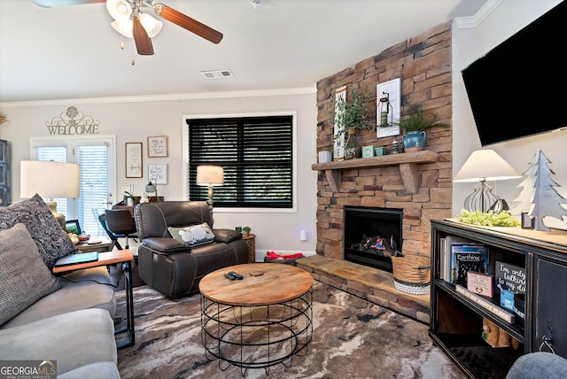 living area with visible vents, ceiling fan, crown molding, and a stone fireplace