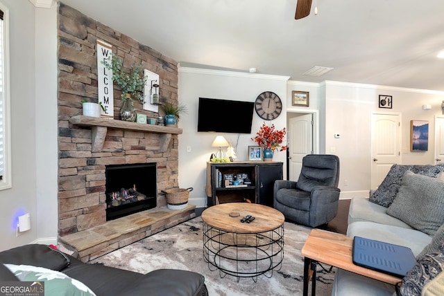 living room featuring baseboards, ornamental molding, ceiling fan, and a stone fireplace