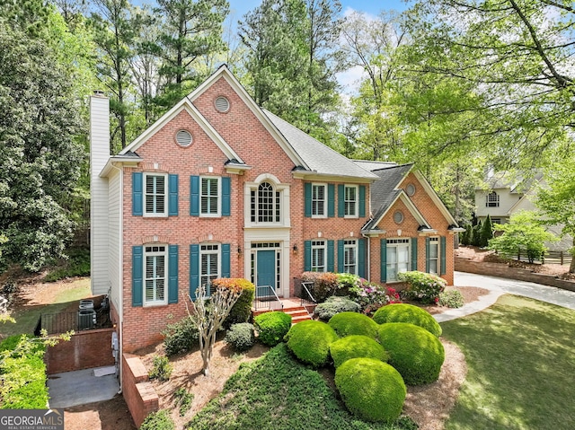 colonial house featuring a chimney, brick siding, cooling unit, and a shingled roof