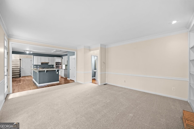 unfurnished living room featuring carpet floors, baseboards, and ornamental molding