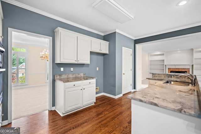 kitchen with white cabinets, dark wood-style floors, a sink, light stone countertops, and baseboards