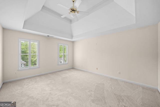 empty room featuring ceiling fan, light carpet, a tray ceiling, and baseboards