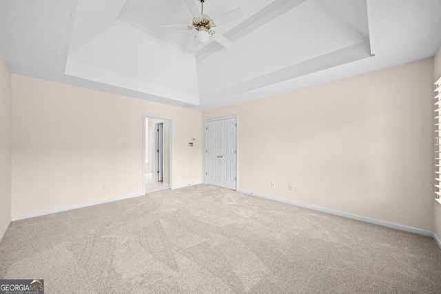 empty room with a raised ceiling, carpet flooring, baseboards, and ceiling fan