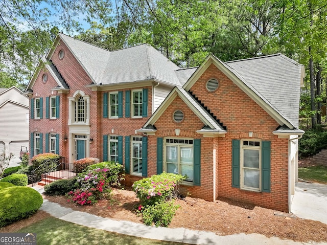 colonial home featuring brick siding and roof with shingles