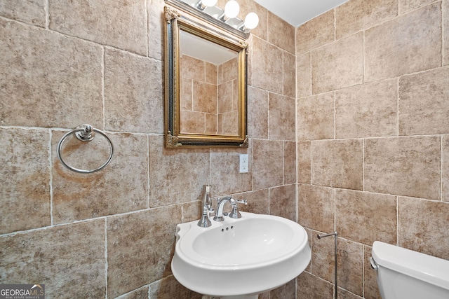 half bath featuring tile walls, toilet, and a sink