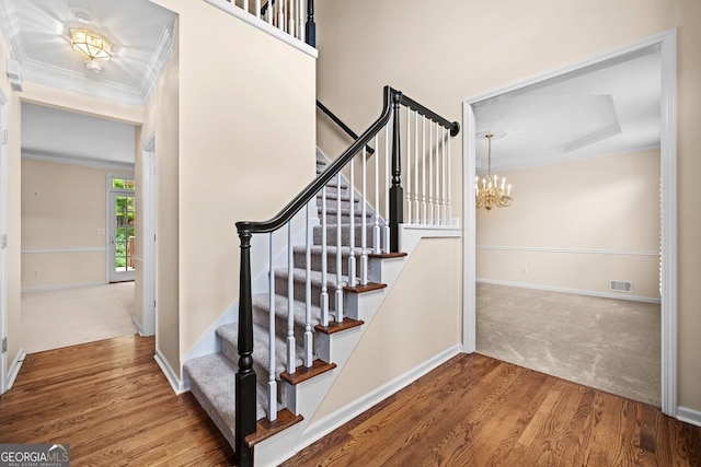 stairway featuring an inviting chandelier, wood finished floors, visible vents, crown molding, and baseboards