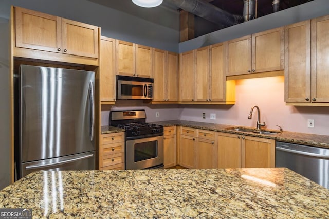 kitchen with light brown cabinetry, light stone counters, a sink, and stainless steel appliances