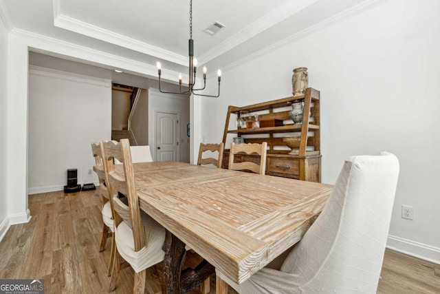 dining space featuring a raised ceiling, ornamental molding, light wood-style floors, and visible vents
