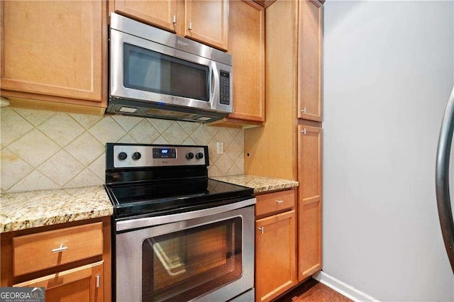 kitchen with baseboards, light stone counters, backsplash, and stainless steel appliances