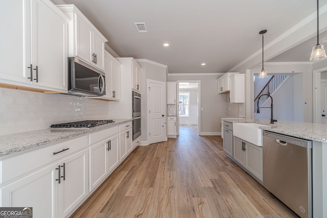 kitchen featuring appliances with stainless steel finishes, a sink, light wood-style flooring, backsplash, and white cabinets