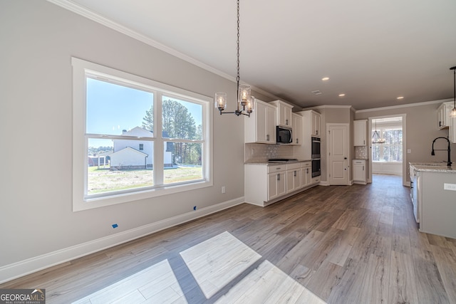 kitchen with a chandelier, appliances with stainless steel finishes, ornamental molding, light wood-style flooring, and white cabinetry