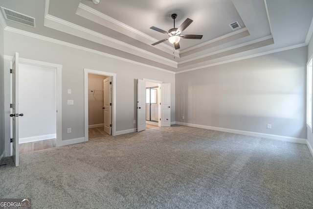 unfurnished bedroom featuring a raised ceiling, light colored carpet, ornamental molding, a spacious closet, and baseboards