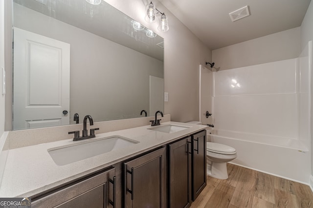 bathroom with wood finished floors, toilet, double vanity, and washtub / shower combination