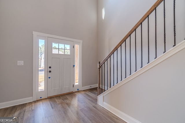foyer entrance featuring stairway, baseboards, wood finished floors, and a towering ceiling