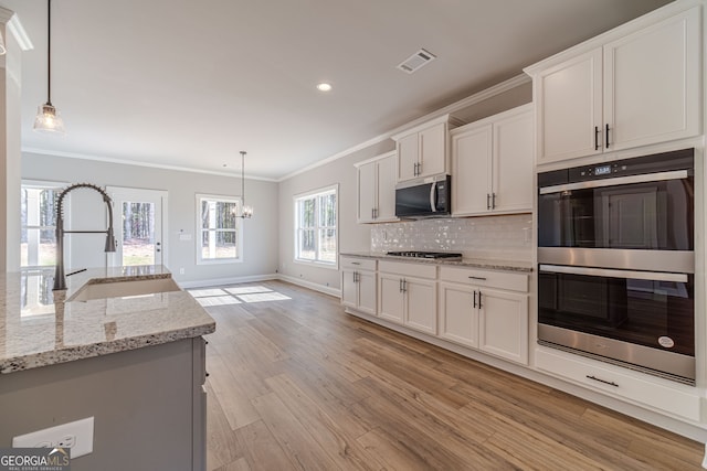 kitchen featuring appliances with stainless steel finishes, ornamental molding, a sink, light wood-style floors, and white cabinetry