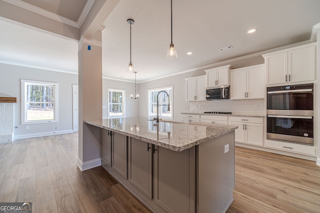 kitchen with stainless steel appliances, a sink, light wood finished floors, light stone countertops, and tasteful backsplash