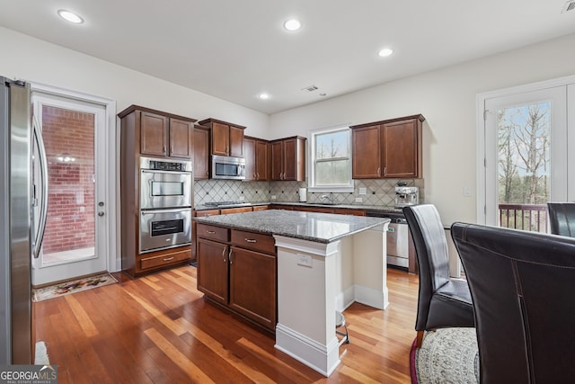 2220 Stirling Bridge Rd, Cumming, GA 30041 - kitchen featuring dark stone counters, stainless steel appliances, a kitchen island, light wood-type flooring, and backsplash