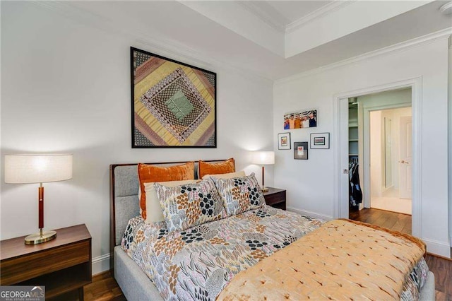bedroom featuring baseboards, ornamental molding, wood finished floors, and a tray ceiling