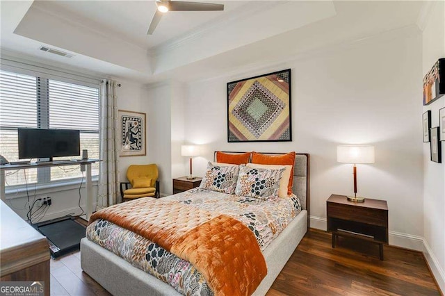 bedroom featuring a tray ceiling, baseboards, visible vents, and wood finished floors